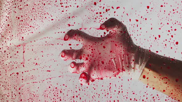 Close-up. Bloody hand in medical glove behind clear glass in drops of blood