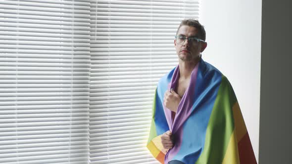 Gay Man Wrapped in Rainbow Flag Posing by Window