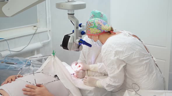 Two Female Surgeons Perform Eye Surgery with Microscope and Medical Instruments
