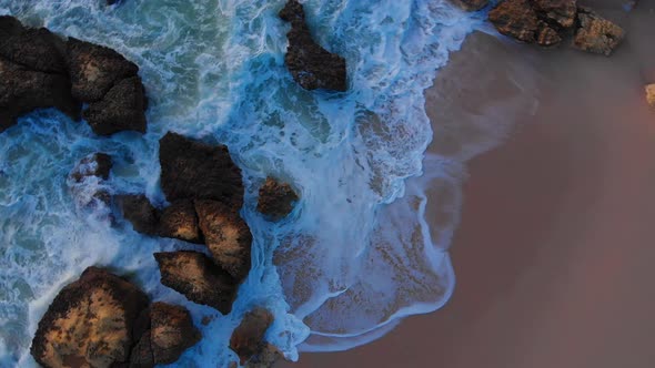 Beautiful aerial drone overhead rotating shot of waves crashing the rocky beach shore