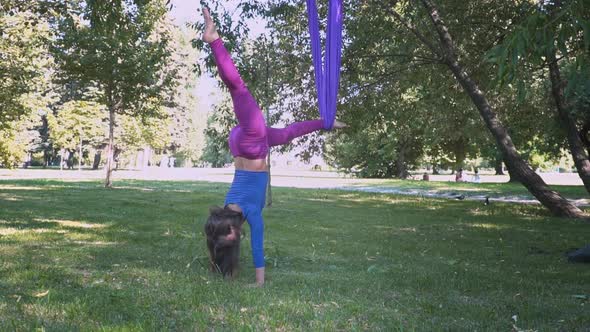 Young Beautiful Sportswear Woman Training Aero Stretch Swing Sunny City Park Hanging Upside Down