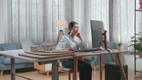 Asian Woman Engineer With The House Model Thinking While Working On A Desktop At Home