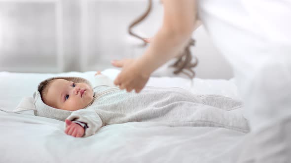 Softness Mother Hand Taking Little Cute Baby Waking Up on Bed Enjoying Morning at White Interior