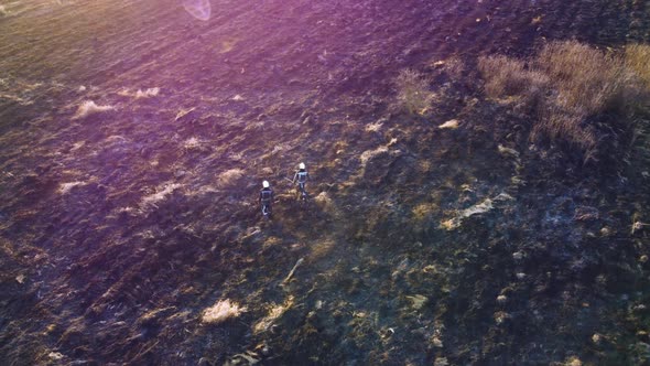 Two Firefighters Walk on Black Scorched Earth After Fire Dry Grass in a Field