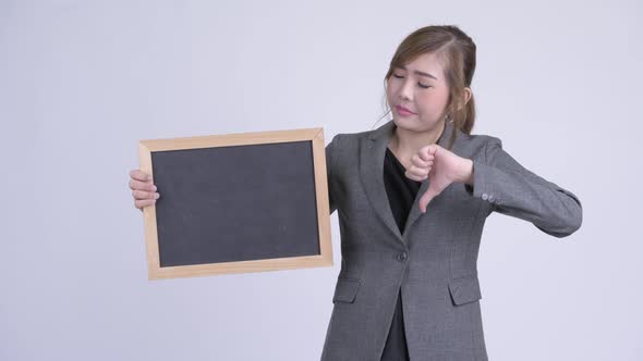 Young Stressed Asian Businesswoman Holding Blackboard and Giving Thumbs Down