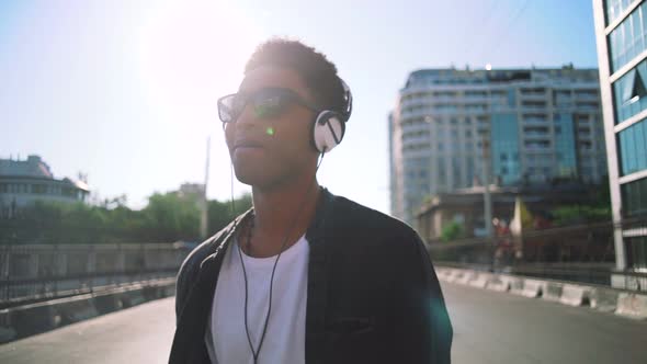 Portrait of Young Stylish Hipster Black Man in White Headphones and Sun Glasses Walking and Dancing