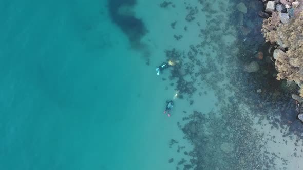 Arial view of three scuba divers swimming underwater following each other using waterproof torches