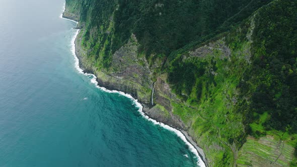 Elevated drone view of cascading waterfall on rocky shoreline; Madeira