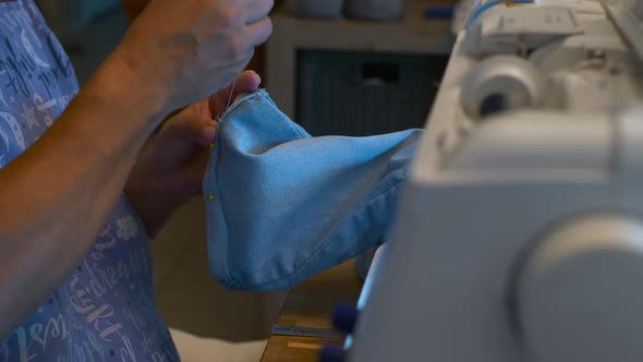 A seamstress threads a needle through a garment next to her sewing machine