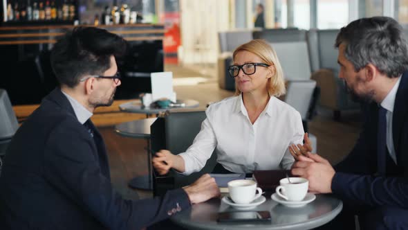 Smiling Businesswoman Discussing Work with Male Partners During Meeting in Cafe