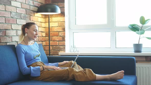 Young Woman Sitting on Sofa with Laptop