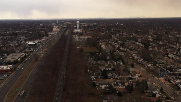 An aerial view of an empty railroad tracks. Residential homes are on the right, a highway, businesse