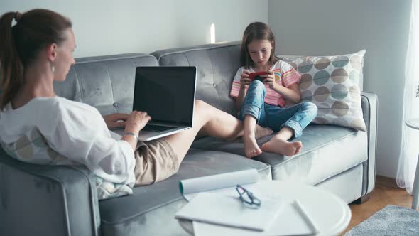 Young Woman Working From Home, While Her Daughter Lying on a Couch