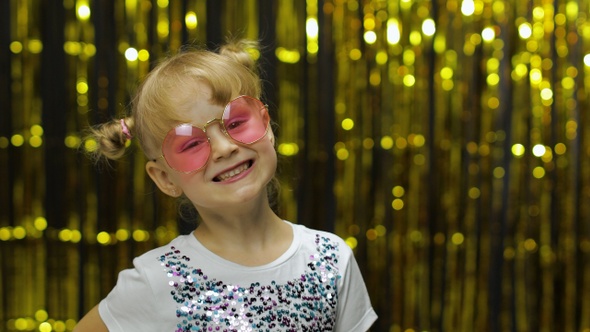 Child Smiling, Looking at Camera. Girl in Pink Sunglasses Posing on Background with Foil Curtain