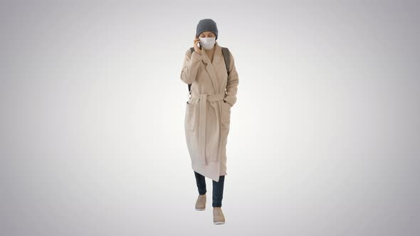 Young Woman in Protective Mask Walking and Talking By Mobile Phone on Gradient Background