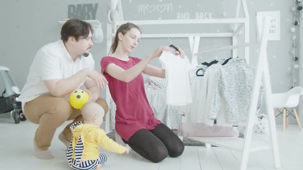 Young Mom Choosing Clothes for Cute Infant at Home