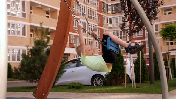 A Little Boy Rides a Swing on a Playground in a Modern Courtyard