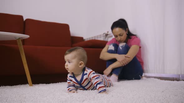 Sad Mother with Arms Around Knees Watching Baby