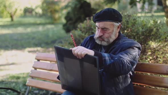 Wrinkled Artist Sits on Street Bench, Begins Smoking and Drawing Picture