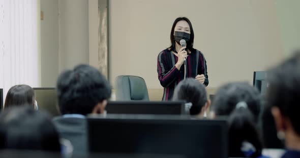 Asian Female Professor With Face Mask Explains To University Student In Classroom.