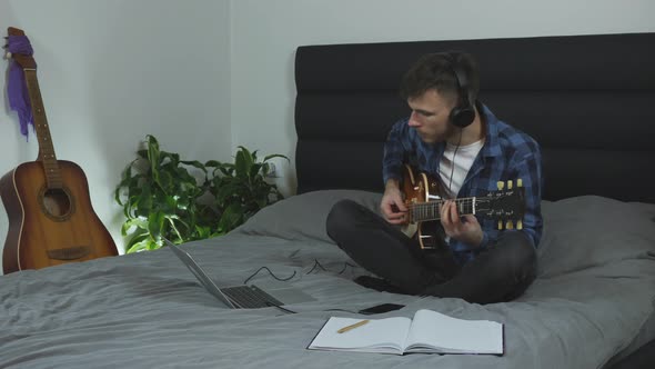 Man in headphones playing guitar solo on bed at home. Music concept
