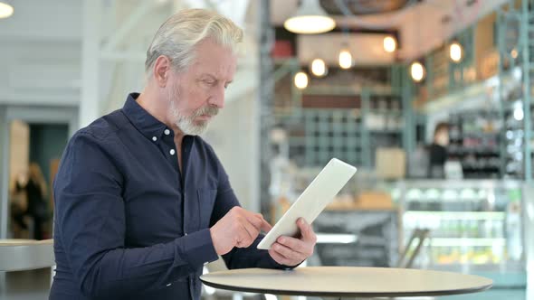 Old Man Using Digital Tablet in Cafe