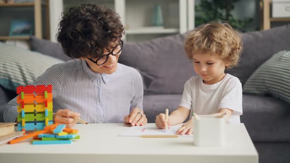 Little Boy Drawing Picture with Pencils While Cheerful Woman Talking and Smiling