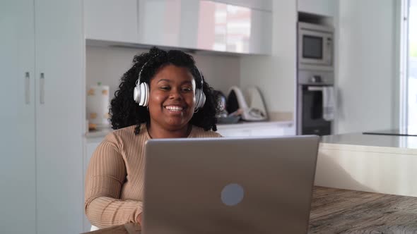 Happy Latin woman having fun doing video call using laptop at home