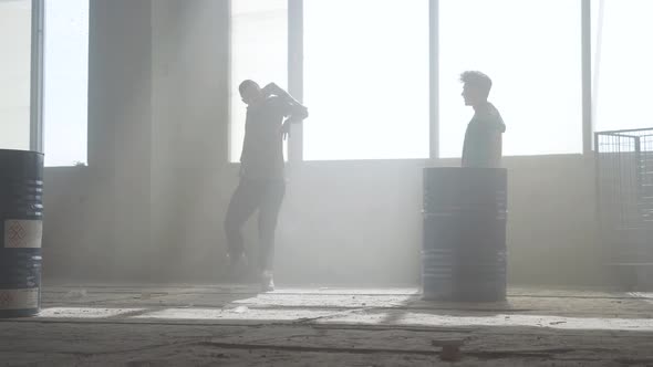 Two Young Men in Casual Clothes in the Dark Dusty Abandoned Building Practicing Dancing