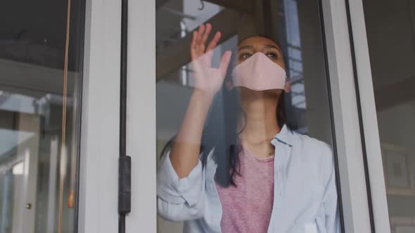 Mixed race woman wearing mask at home looking through window