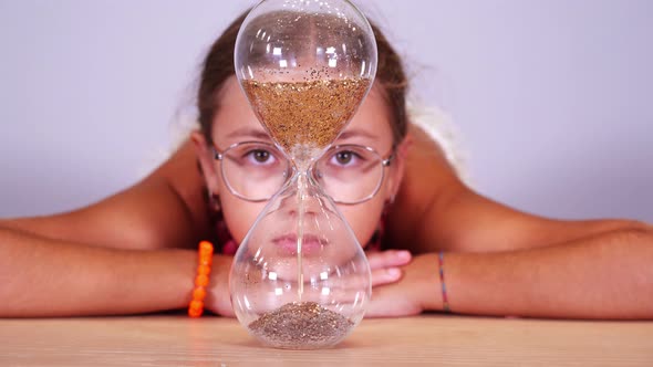 Teenage Girl Looks at Sand Pouring Down Inside Hourglass