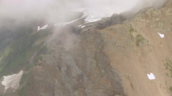 Slow panning look down a mountain top and sheer cliffs onto a meadow and lake below.