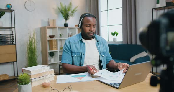 Man in Headset Sitting in front of Camera at Home and Explaining Diagrams