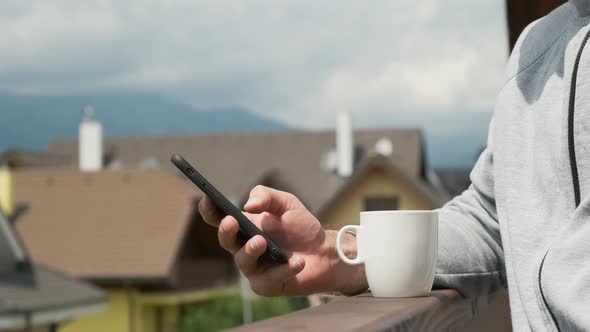 Man Using His Smartphone on the Background of Mountains and New Houses.