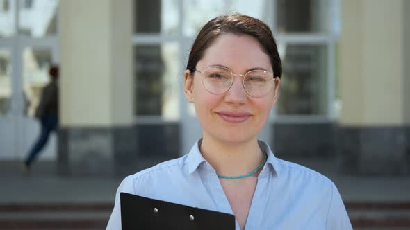 A Young Attractive Female Student with Glasses Looks Into the Camera and Smiles