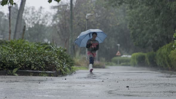 Slow motion of a little girl skipping in puddles holding an umbrella in the rain