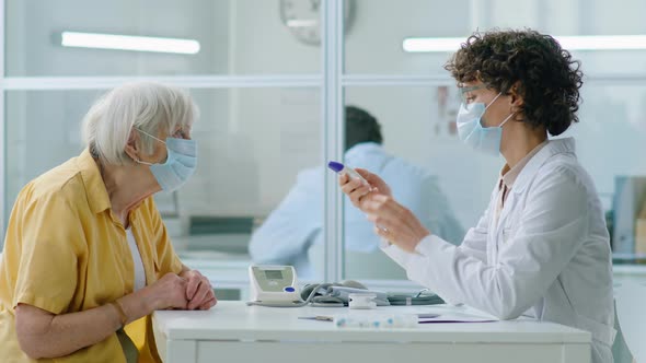 Doctor in Mask Taking Temperature of Senior Woman