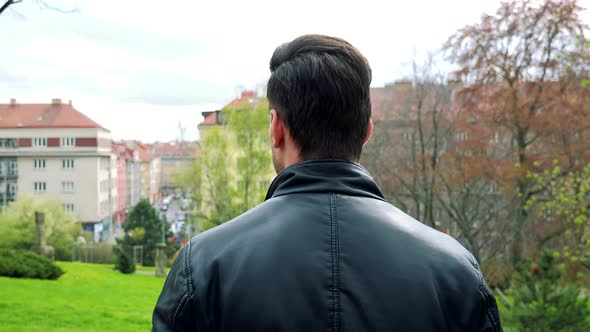 Young Handsome Man Stands and Observes Landscape in Park - Detail From Behind