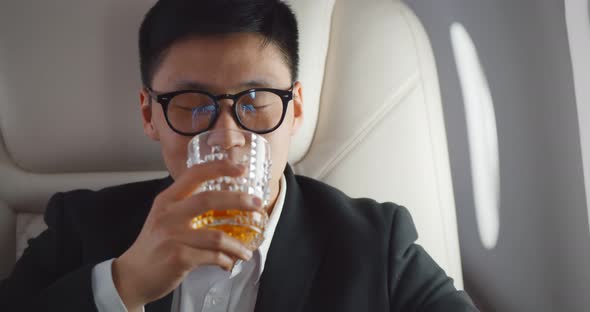 Close Up of Asian Businessman Drinking Whiskey in Glass in Plane