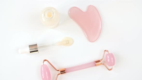 Rotation of Pink Quartz Facial Roller and Glass Bottle with Pipette with Gel Fluid Collagen Serum