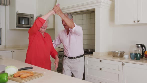 Happy caucasian senior couple having fun dancing in kitchen while preparing meal