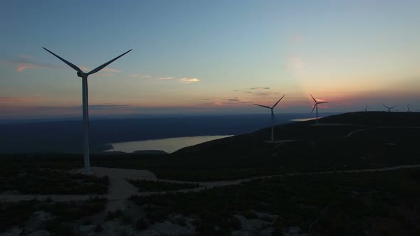 Flying above group of white wind turbines at sunset