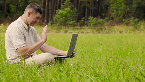 Smiling Man Talking on Video Online Sitting on the Lawn in the Grass