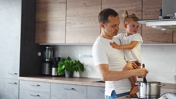 Father with His Daughter on His Hands Cooking Soup Together in Modern Home Kitchen