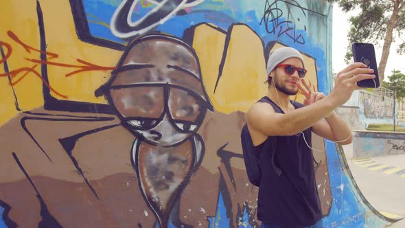 Young boy taking a selfie in a skate park with graffiti on background