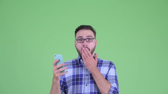 Happy Young Bearded Hipster Man Using Phone and Looking Surprised