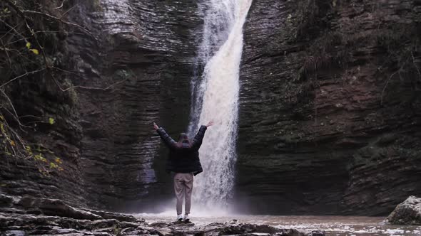 a girl on the background of a waterfall raises her hands