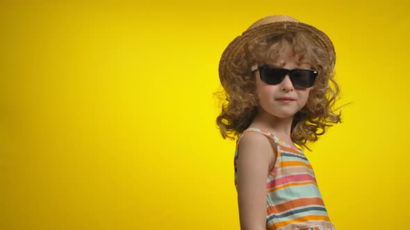 A Cute Little Curly Girl in Sunglasses is Turning Around in a Yellow Background