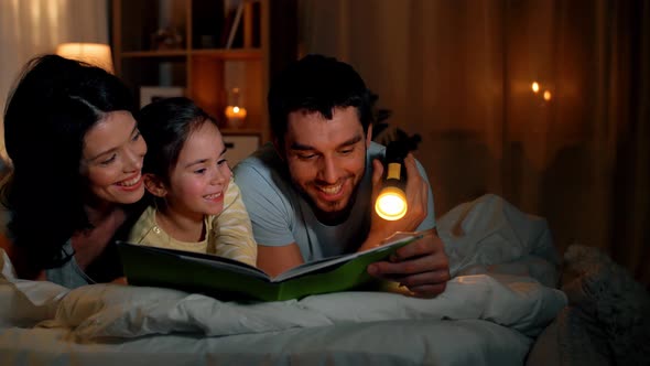Happy Family Reading Book in Bed at Night at Home