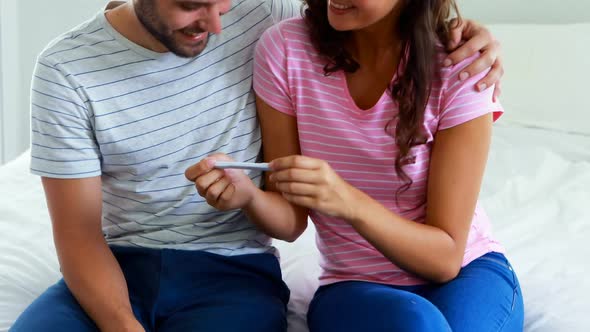 Happy couple looking at pregnancy test on bed in bedroom